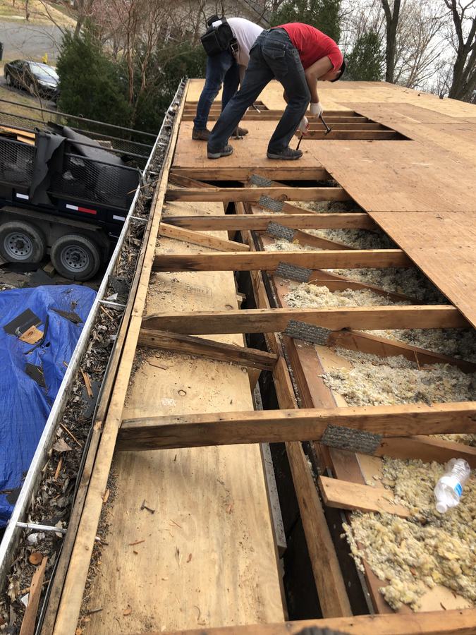 Crew working along the full length of a roof tear-off with a debris-filled gutter along the edge